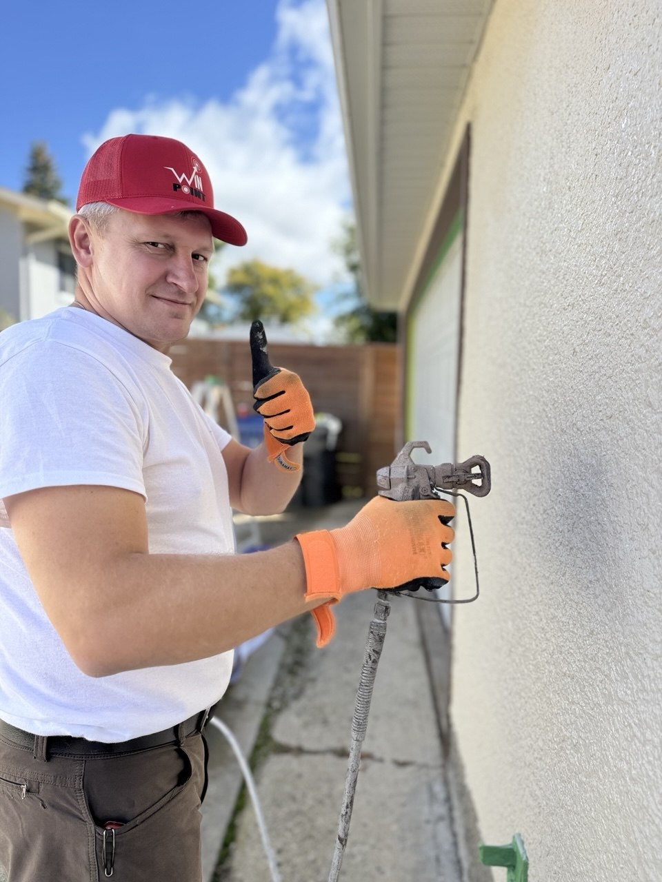 Win Point crew member in a branded cap holding a paint sprayer while working on a residential exterior